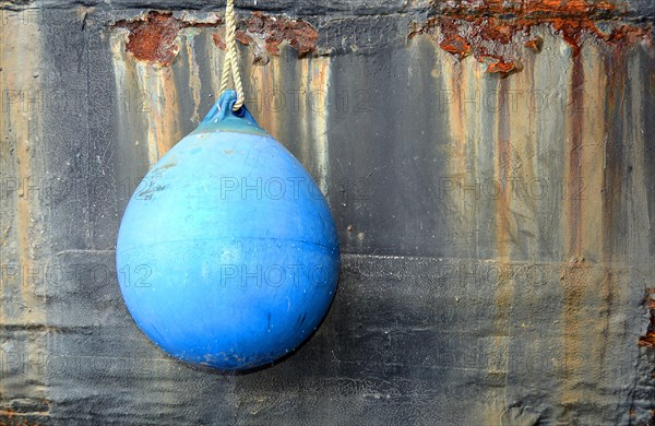 Blue fender in front of rusty ship's wall