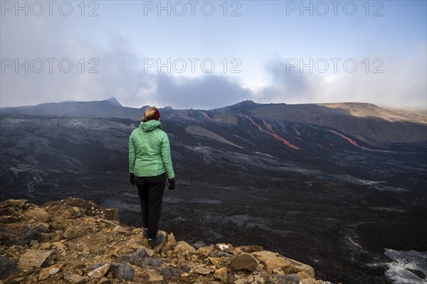 Tourist looking at erupting volcano with lava fountains and lava field