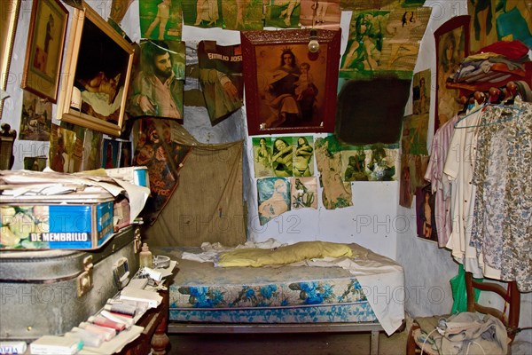 Bedroom with images of saints and photos of woman above bed in a cave dwelling