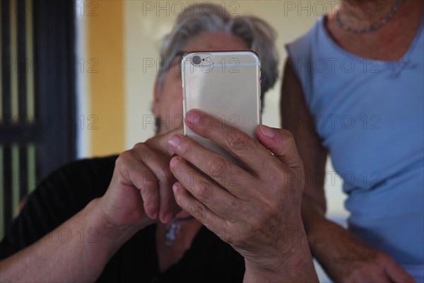 Two older woman help each other with mobile phone operation
