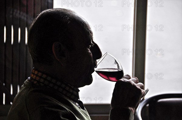 Old man drinking red wine against the light