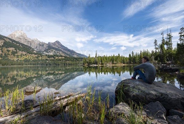Young man sitting on a stone by a lake