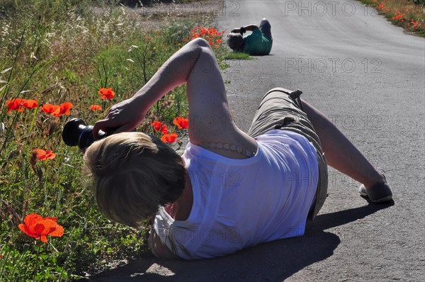 Women lying on the ground photographing poppies