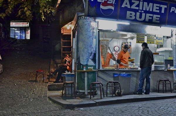Kebab shop illuminated at night with vendor and customers