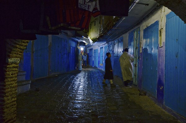 Shopkeepers close door in sparsely lit alley with closed shops at night