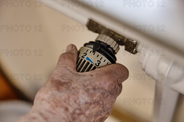 Hand of a senior citizen with age spots on the thermostat of a heater