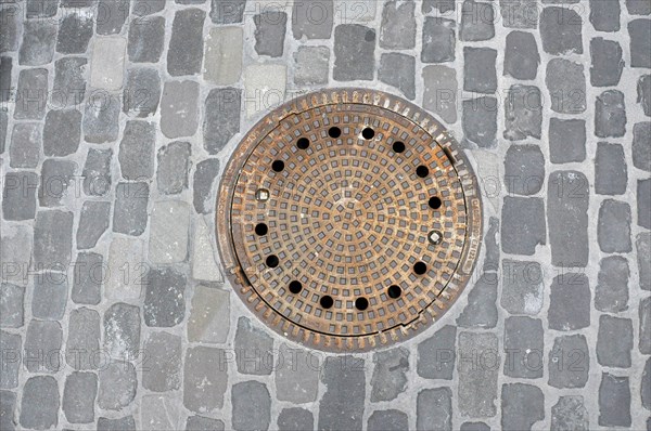 Round iron manhole cover in cobblestones
