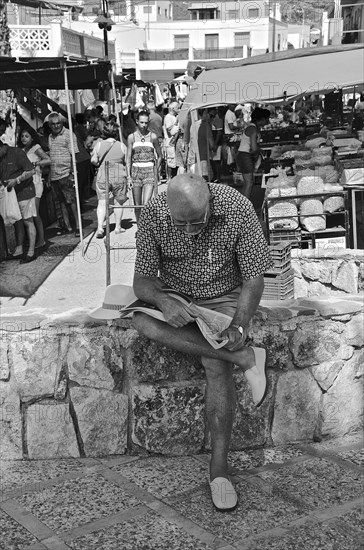 Old man reading newspaper on wall in front of market