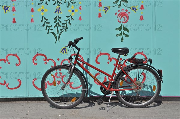 Red bicycle on stand in front of green painted wall with ornaments at Oktoberfest
