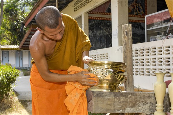 Buddhist monk cleans golden offering bowl in Buddhist monastery