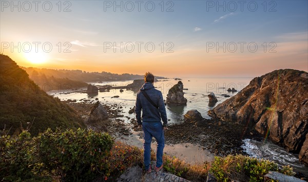Young man looking at the sea and sandy beach Harris Beach with rocks at sunrise