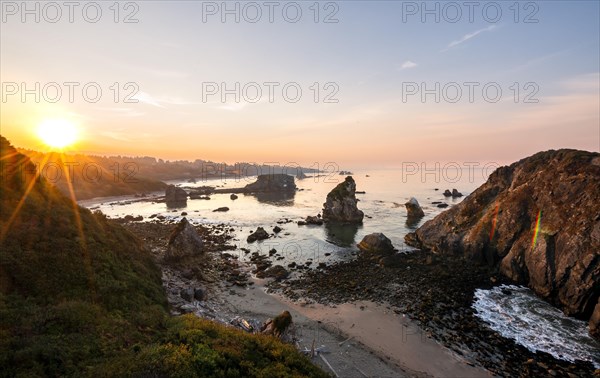 View of sea and sandy beach Harris Beach with rocks at sunrise with sun star