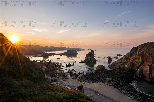 View of sea and sandy beach Harris Beach with rocks at sunrise with sun star