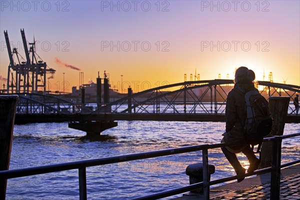 A woman sits on a railing at sunset on the Norderelbe in Altona