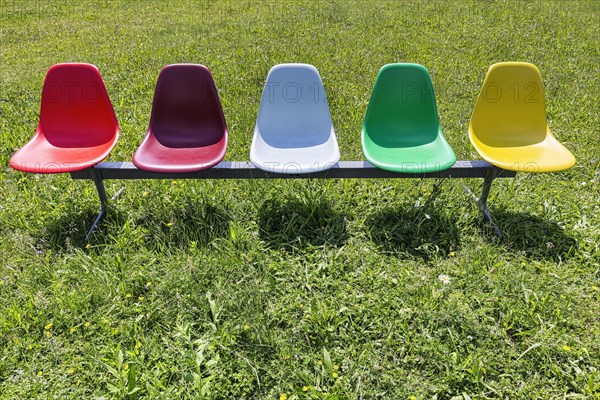 Five colourful plastic chairs in a meadow