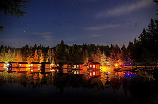 Small wooden holiday cabins at night on the shore of a lake