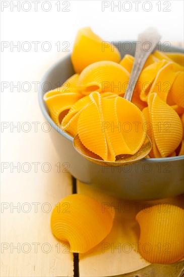 Raw Italian snail lumaconi pasta on a blue bowl over rustic table macro