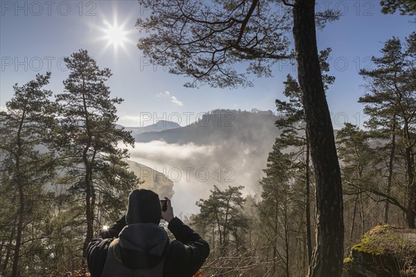 Man taking a photo of the view from the Biedermann Mausoleum into the Elbe Valley with Koenigstein Fortress in the morning mist