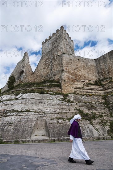 A young men dressed in the attire of one of the numerous brotherhoods of Enna walking in front of the castle of Enna