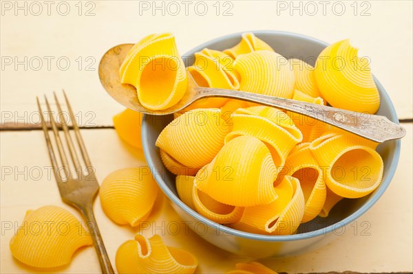 Raw Italian snail lumaconi pasta on a blue bowl over rustic table macro