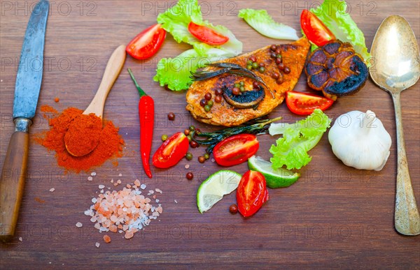Wood fired hoven cooked chicken breast on wood board with herbs spices and vegetables
