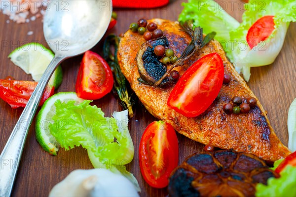 Wood fired hoven cooked chicken breast on wood board with herbs spices and vegetables