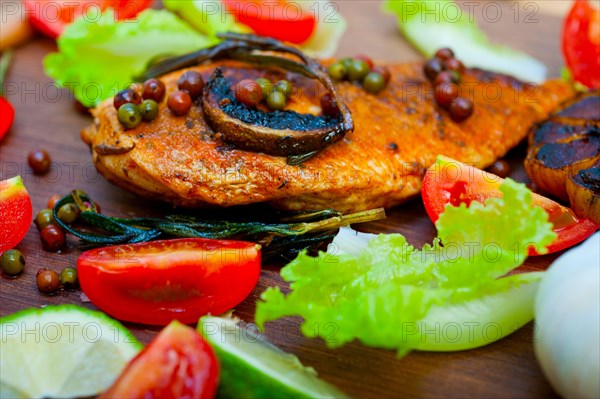 Wood fired hoven cooked chicken breast on wood board with herbs spices and vegetables