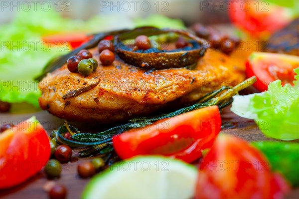 Wood fired hoven cooked chicken breast on wood board with herbs spices and vegetables