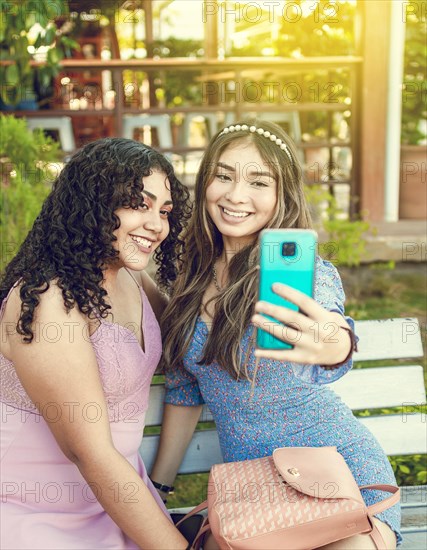Two pretty girls sitting on a bench taking a selfie