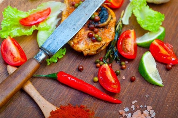 Wood fired hoven cooked chicken breast on wood board with herbs spices and vegetables