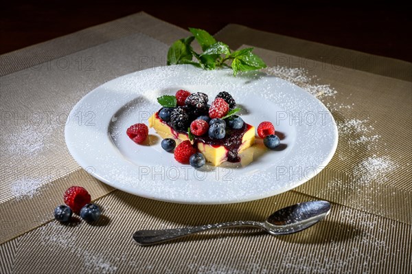 A slice of cheesecake with fresh raspberries and blackberries and a layer of icing sugar on a white plate
