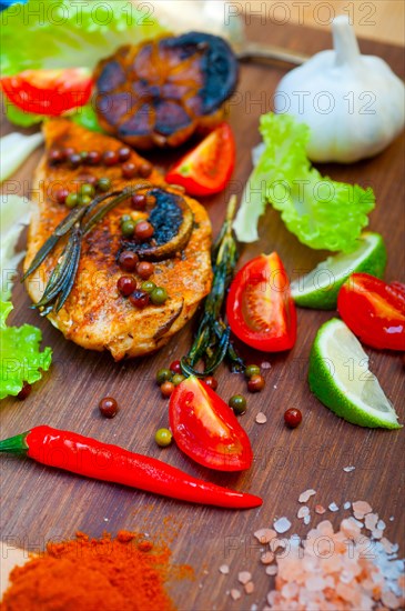 Wood fired hoven cooked chicken breast on wood board with herbs spices and vegetables
