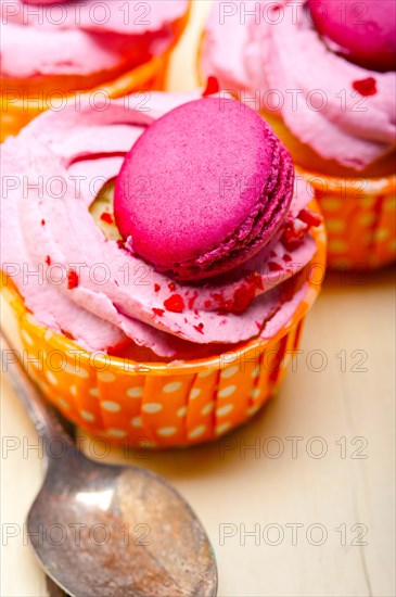 Fresh pink berry cream cupcake with macaroon on top over rustic wood table
