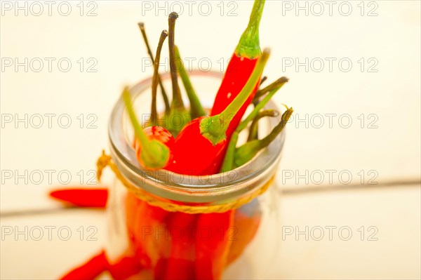Red chili peppers on a glass jar over white wood rustic table