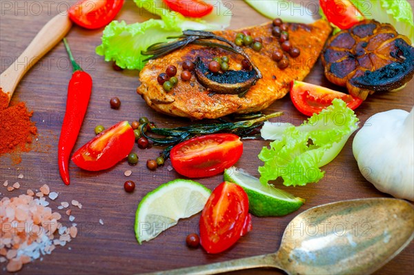 Wood fired hoven cooked chicken breast on wood board with herbs spices and vegetables