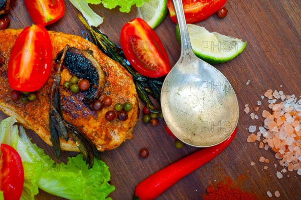 Wood fired hoven cooked chicken breast on wood board with herbs spices and vegetables