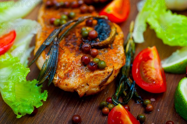 Wood fired hoven cooked chicken breast on wood board with herbs spices and vegetables