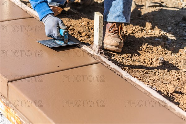 Construction worker using stainless steel edger on wet cement forming coping around new pool
