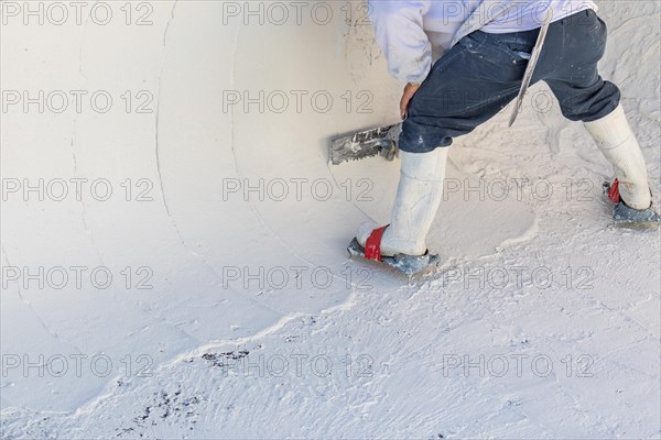 Worker wearing spiked shoes smoothing wet pool plaster with trowel