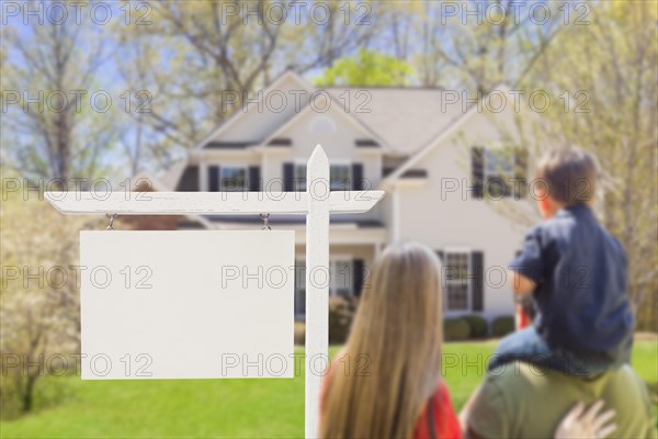mixed-race young family in front of blank real estate sign and new house