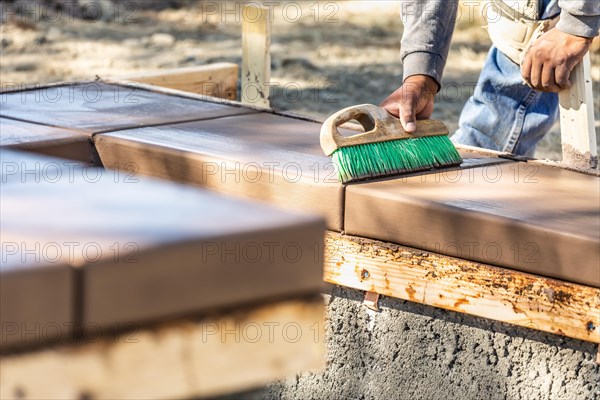 Construction worker using brush on wet cement forming coping around new pool
