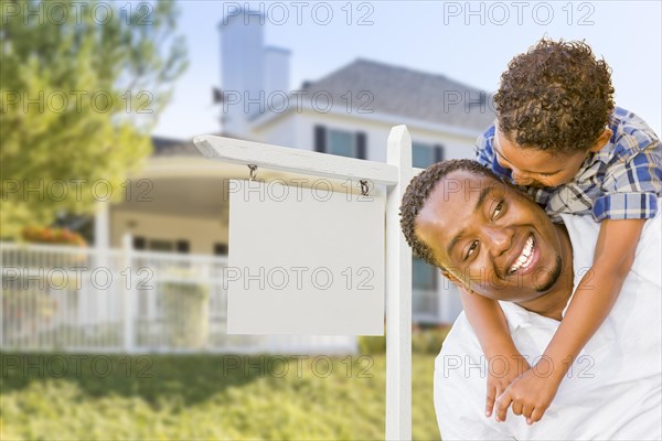 Happy african american father and mixed-race son in front of blank real estate sign and new house