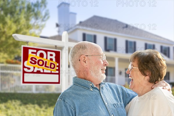 Happy affectionate senior couple hugging in front of sold real estate sign and house