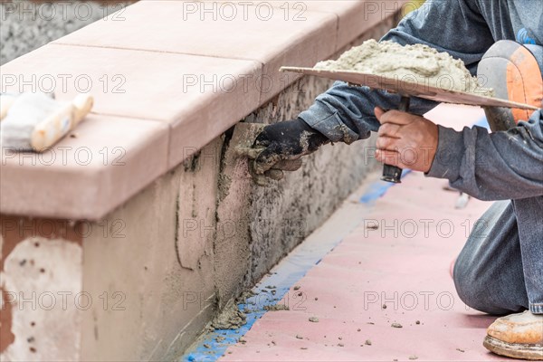 Tile worker applying cement with trowel at pool construction site