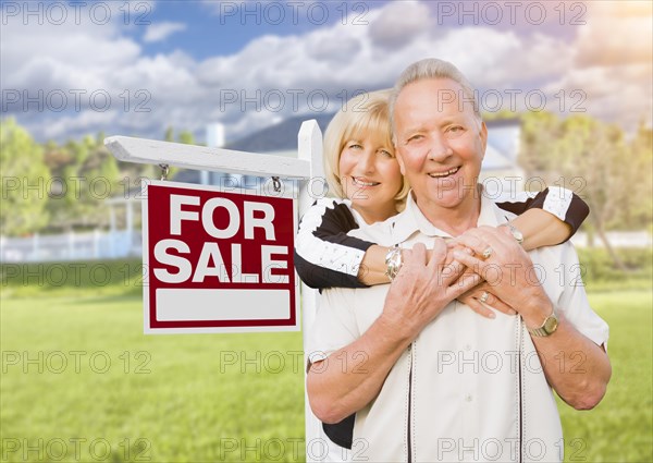 Happy senior couple front of for sale real estate sign and house