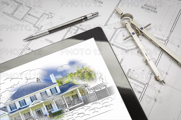 Computer tablet showing house illustration sitting on house plans with pencil and compass