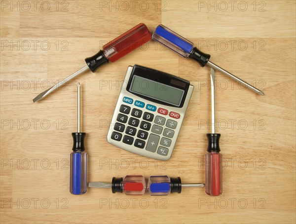 House shaped by screwdrivers and calculator on a wood background