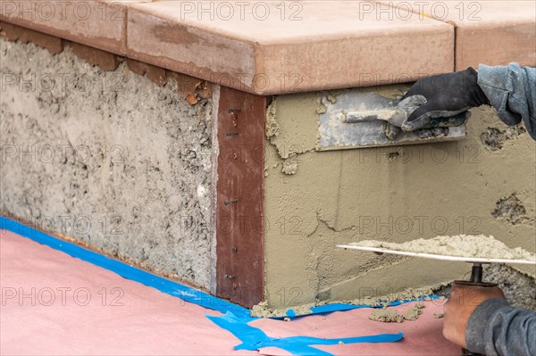 Tile worker applying cement with trowel at pool construction site