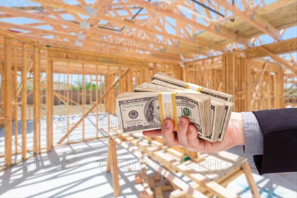 Hand with stacks of cash on site inside new home construction framing