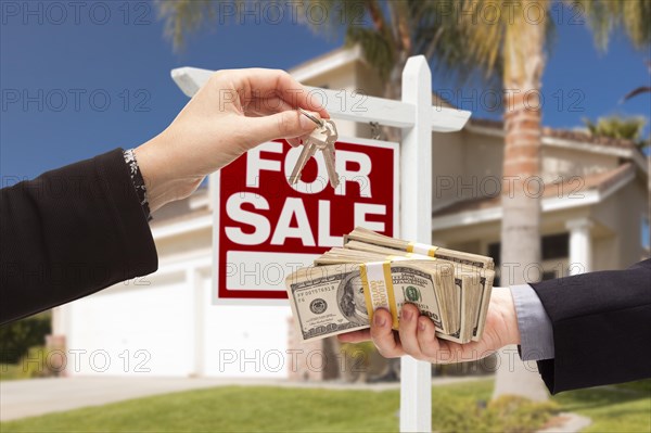 Agent handing over keys as buyer is handing over cash for house with home and for sale real estate sign behind